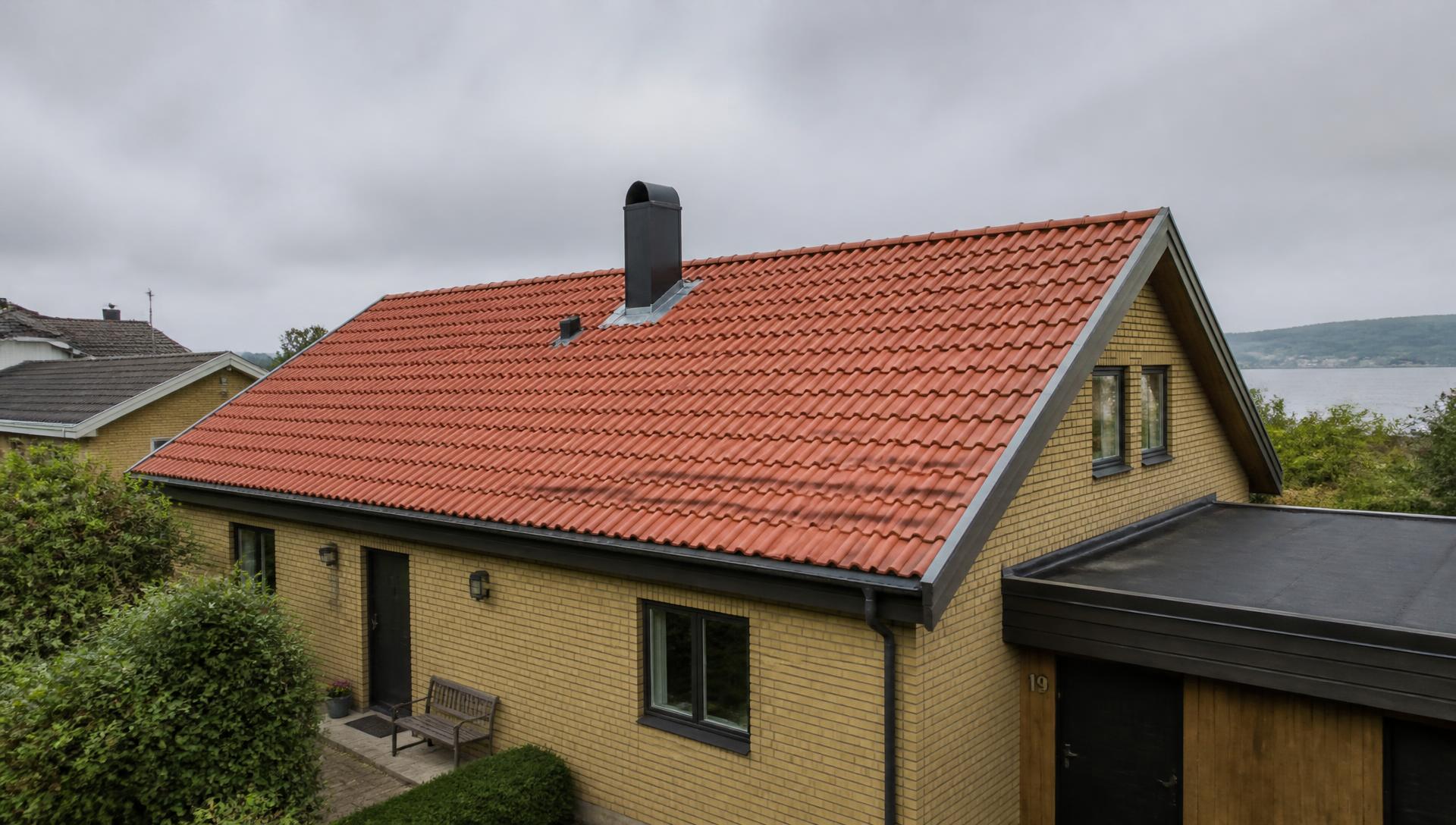 Illustrationsbild av ett bostadshus med tegeltak, skorsten och plåtdetaljer